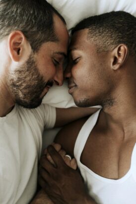 Two men holding hands, laying down and touching forheads